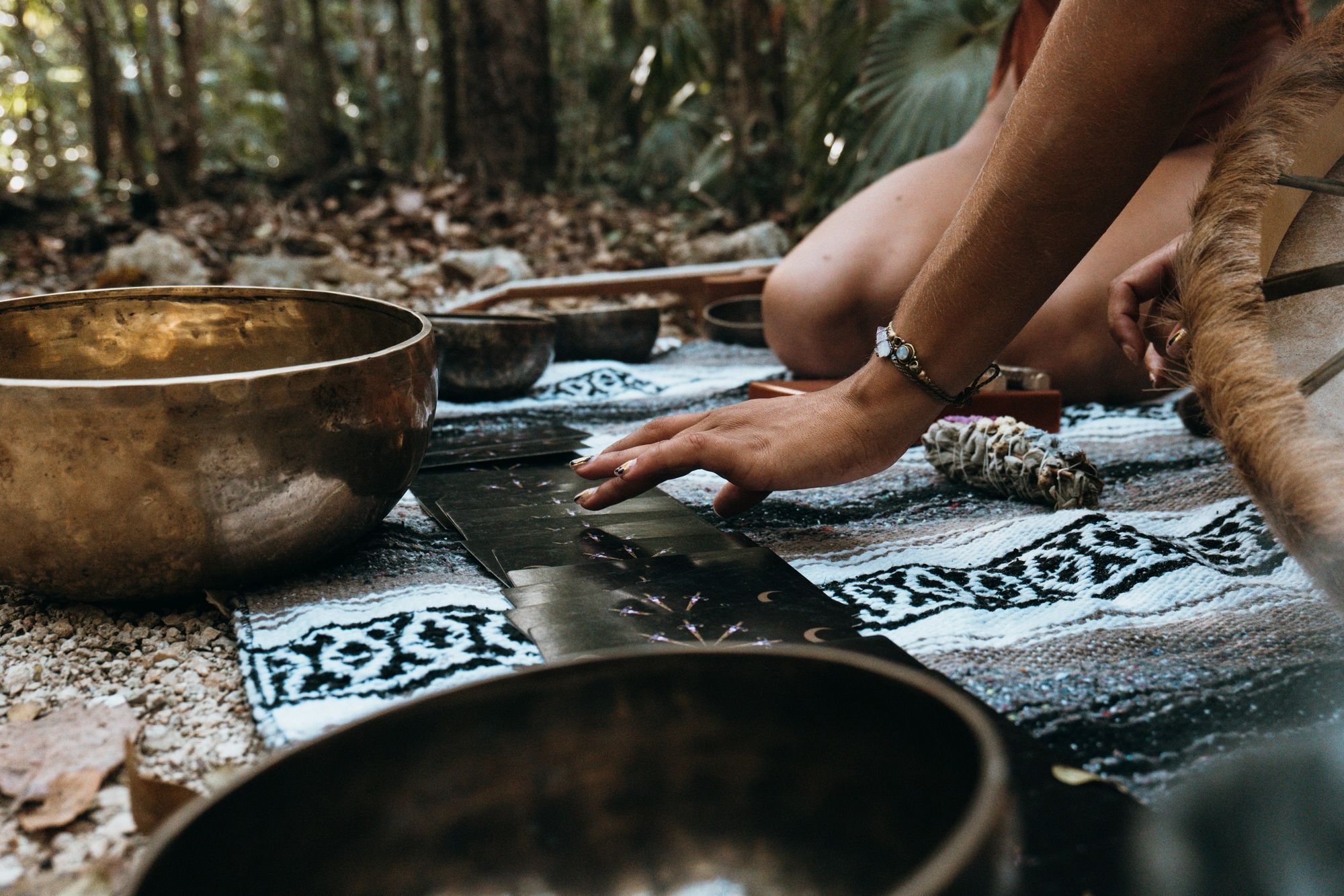 Person engaging in a spiritual tarot reading outdoors with singing bowls nearby.