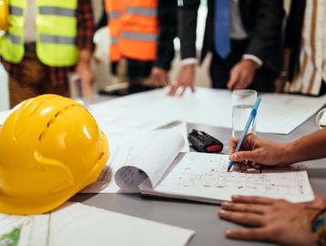 Engineers working on building plans with a yellow safety helmet on the table.