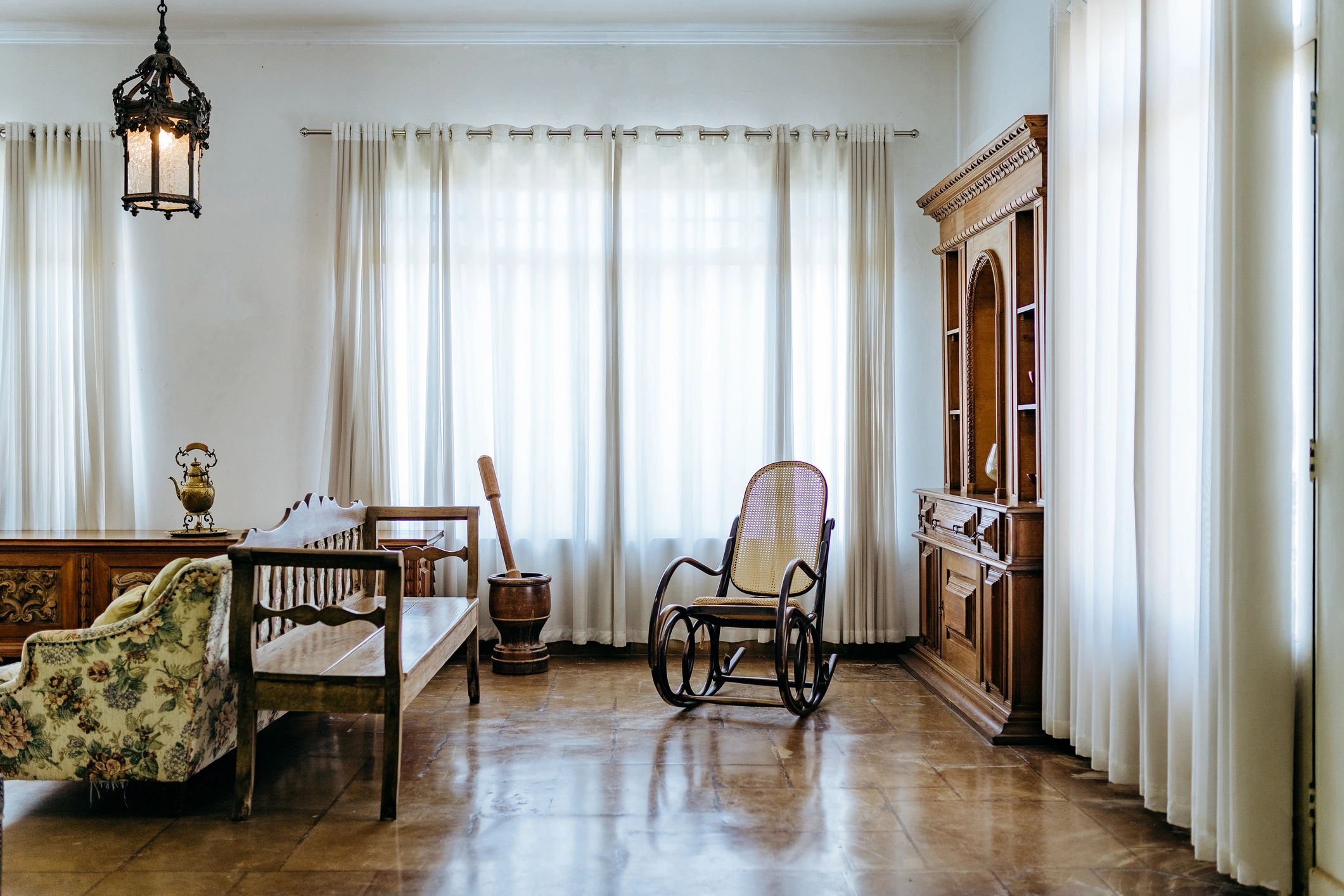Vintage living room with wooden furniture and sheer white curtains.