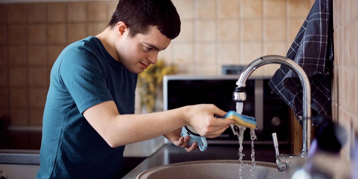 Young man washing a mug in a kitchen sink with running water.