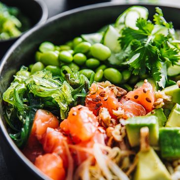 A colorful poke bowl with fresh salmon, avocado, seaweed, and edamame.