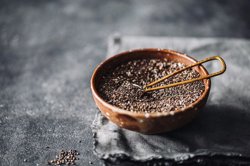 Chai seeds in a bowl on a kitchen coutner. Healthy Chia seeds in a ceramic bowl with spoon on black table.
