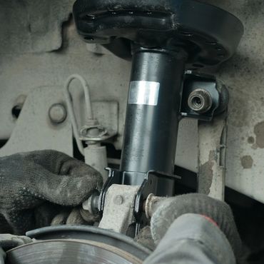A mechanic wearing gloves working on a vehicle suspension component.