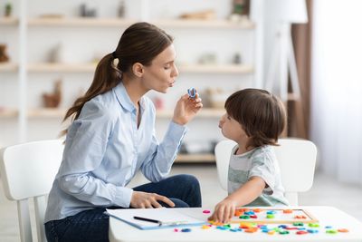 Woman teaching a child to pronounce the letter U using colorful magnets.