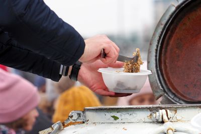 A person serving food from a large container into a bowl outdoors.