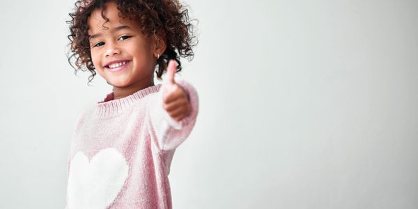 Smiling child giving a thumbs up while wearing a pink sweater with a heart.