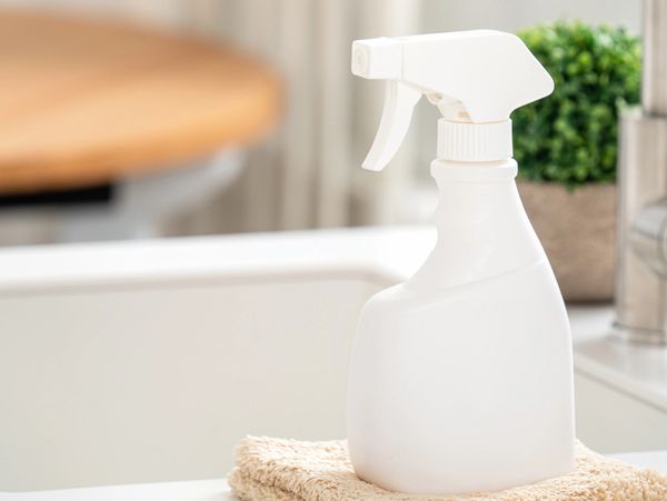 White spray bottle on a beige cloth in a clean kitchen setting.