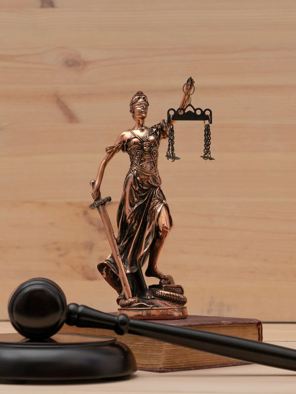 Bronze Lady Justice statue beside a gavel and a law book on a wooden surface.