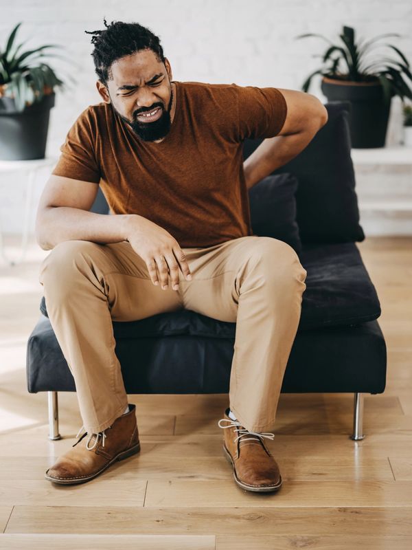 Man sitting on couch holding his lower back in pain.