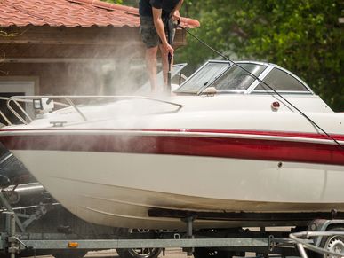 Person pressure washing the front of a white and red boat.