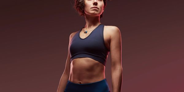 Fit woman in athletic wear posing confidently with dramatic lighting.