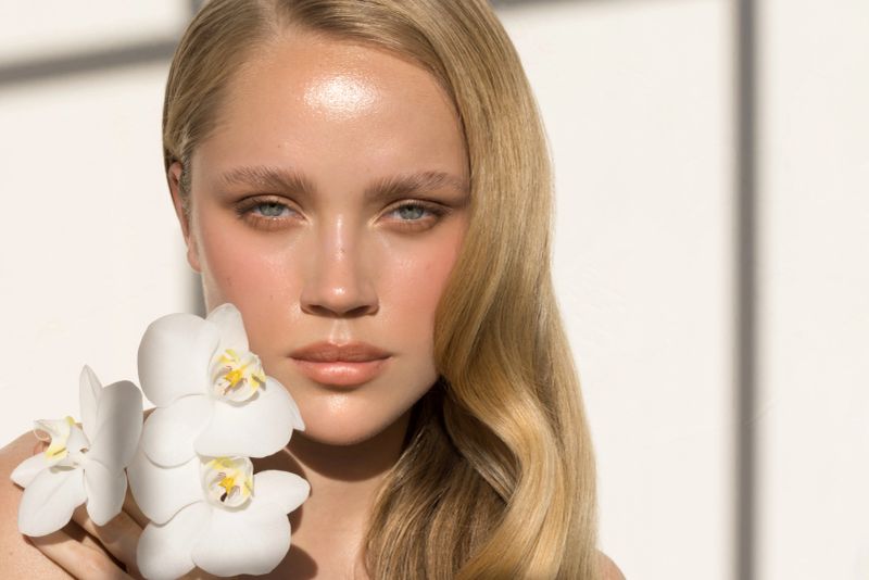 Close up studio shot of a beautiful natural blonde woman, holding orchid flower. Natural sunlight.