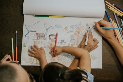 Overhead view of a child and adult drawing together with coloured pencils.