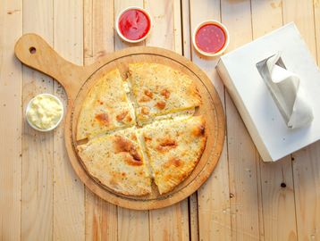 Four sliced cheesy stuffed flatbreads on a wooden board with three sauces and a tissue box.