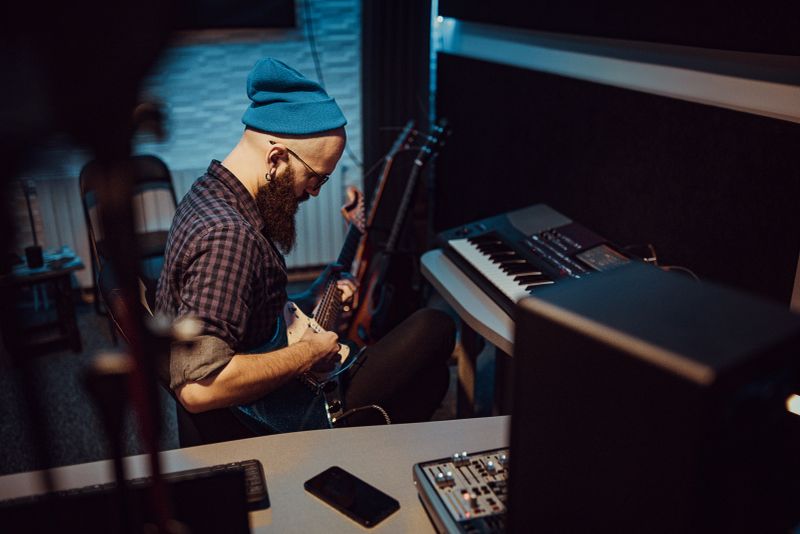 Young man playing electric guitar in the control room of the recording music studio