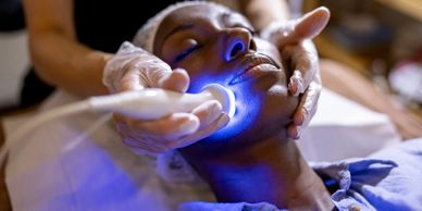 Woman receiving a blue light facial treatment at a spa.