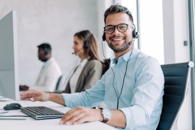 Smiling man with headset working at computer in call center.