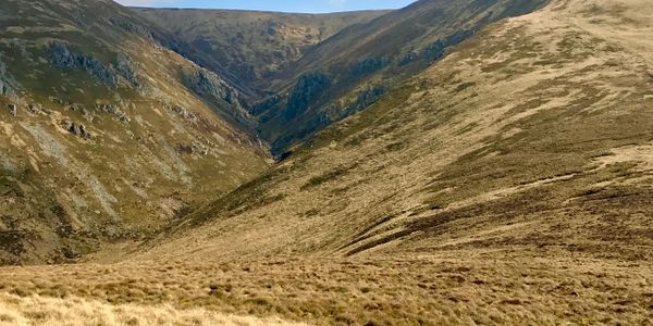 A vast, grassy mountain valley with rugged slopes and a clear blue sky.