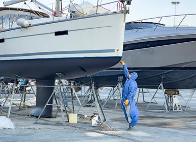 Person in protective suit inspecting a boat on dry dock.
