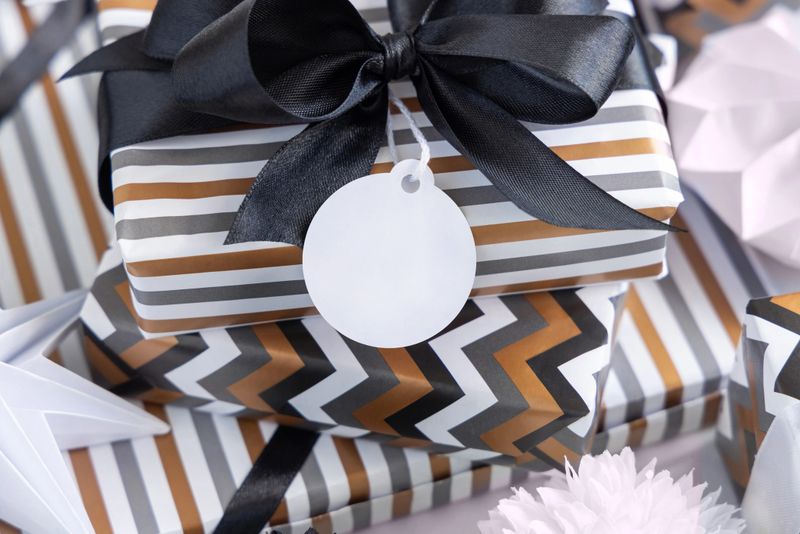 Present with round blank gift tag and black bow close up. Gift boxes wrapped in Striped and chevron geometric paper near black and white decor. Christmas, New Year, Birthday, Anniversary label mockup