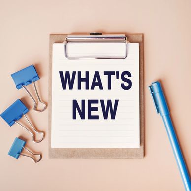 Clipboard with 'WHAT'S NEW' text, blue binder clips, and a pen on a beige background.