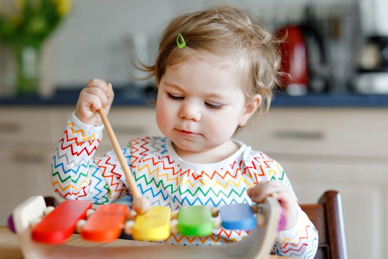 Adorable cute beautiful little baby girl playing with educational wooden music toy at home. Happy excited toddler child learn to play colorful rainbow xylophon. Early education, activity for children