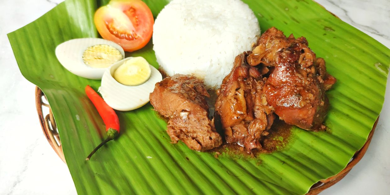 Rice, stewed chicken, hard-boiled egg, tomato, and chili on a banana leaf.
