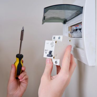 Person installing a circuit breaker with a screwdriver in an electrical panel.