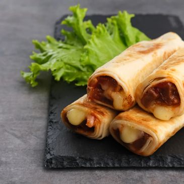 Cheese-filled rolled snacks on a slate plate with leafy greens.