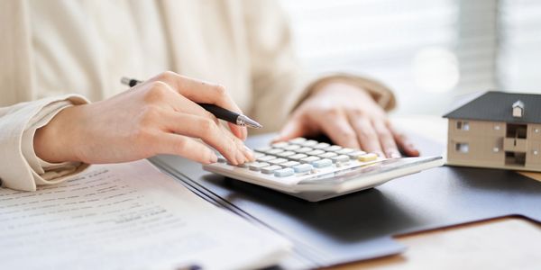 Person using calculator with documents and house model nearby.