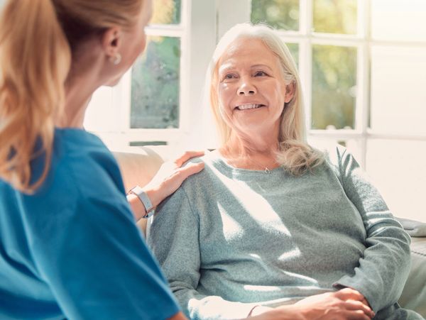 Caregiver comforting a smiling elderly woman in a sunlit room.