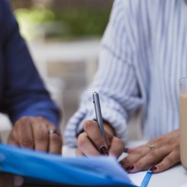 Two people writing on a document with a pen.
