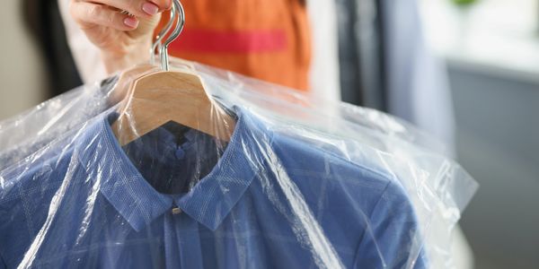 A blue shirt on a wooden hanger covered with plastic at a dry cleaner.