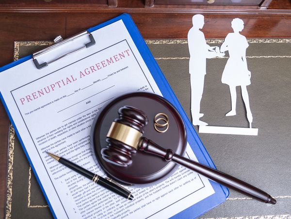 Prenuptial agreement with gavel, wedding rings, and paper cutout of couple on desk.