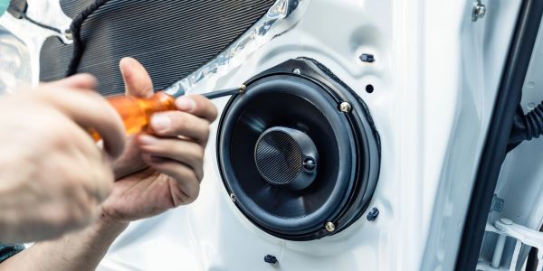 Person installing a car speaker inside a vehicle door.