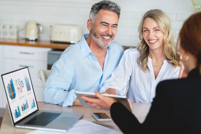 Smiling middle-aged couple at desk with an advisor reviewing IPad