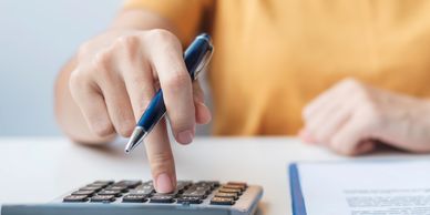 Person in yellow shirt using calculator and holding pen while reviewing documents.