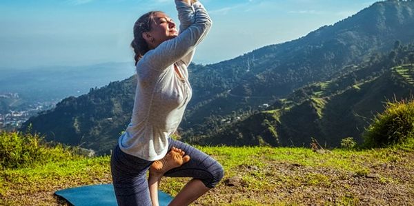 Woman practicing yoga on a mat outdoors with scenic mountain views.
