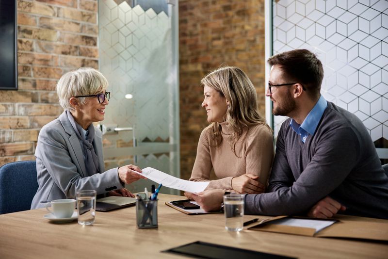 Happy senior agent giving her customer paperwork while having a meeting in the office. Focus is on women.