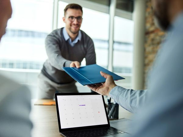 Man handing over a blue folder in a business meeting.