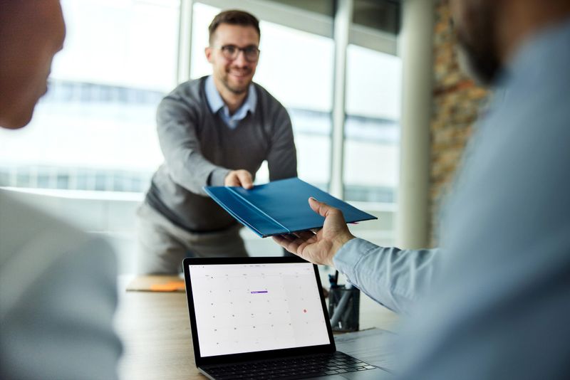 Male candidate giving his paperwork to human resource team on a job interview in the office.