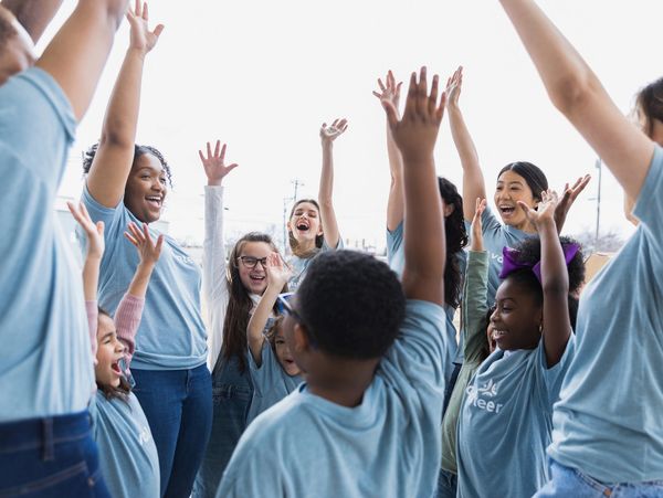 A diverse group of adults and children cheering with their hands raised.