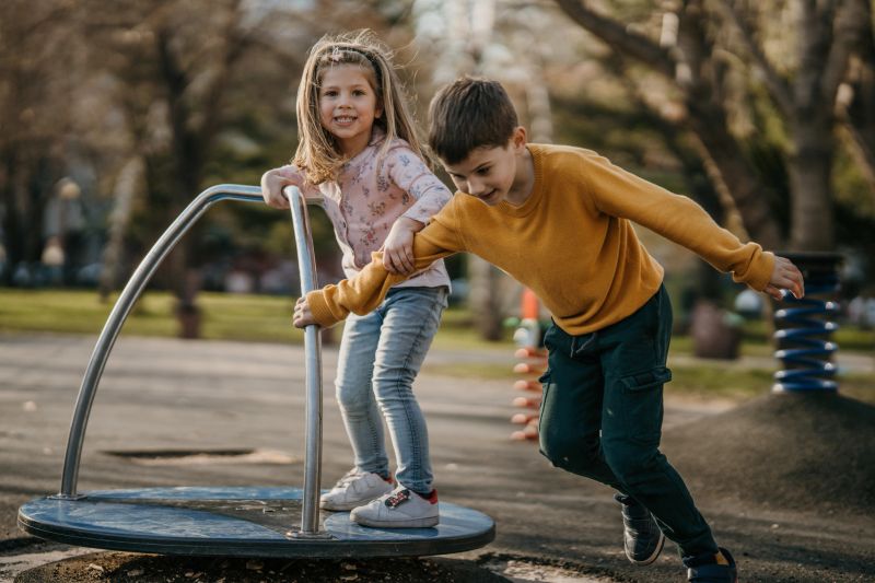 Cute little girl and her older brother playing in public park playground together.