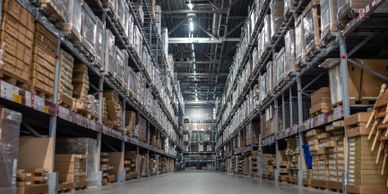 A wide aisle between tall shelves stocked with boxed goods in a warehouse.