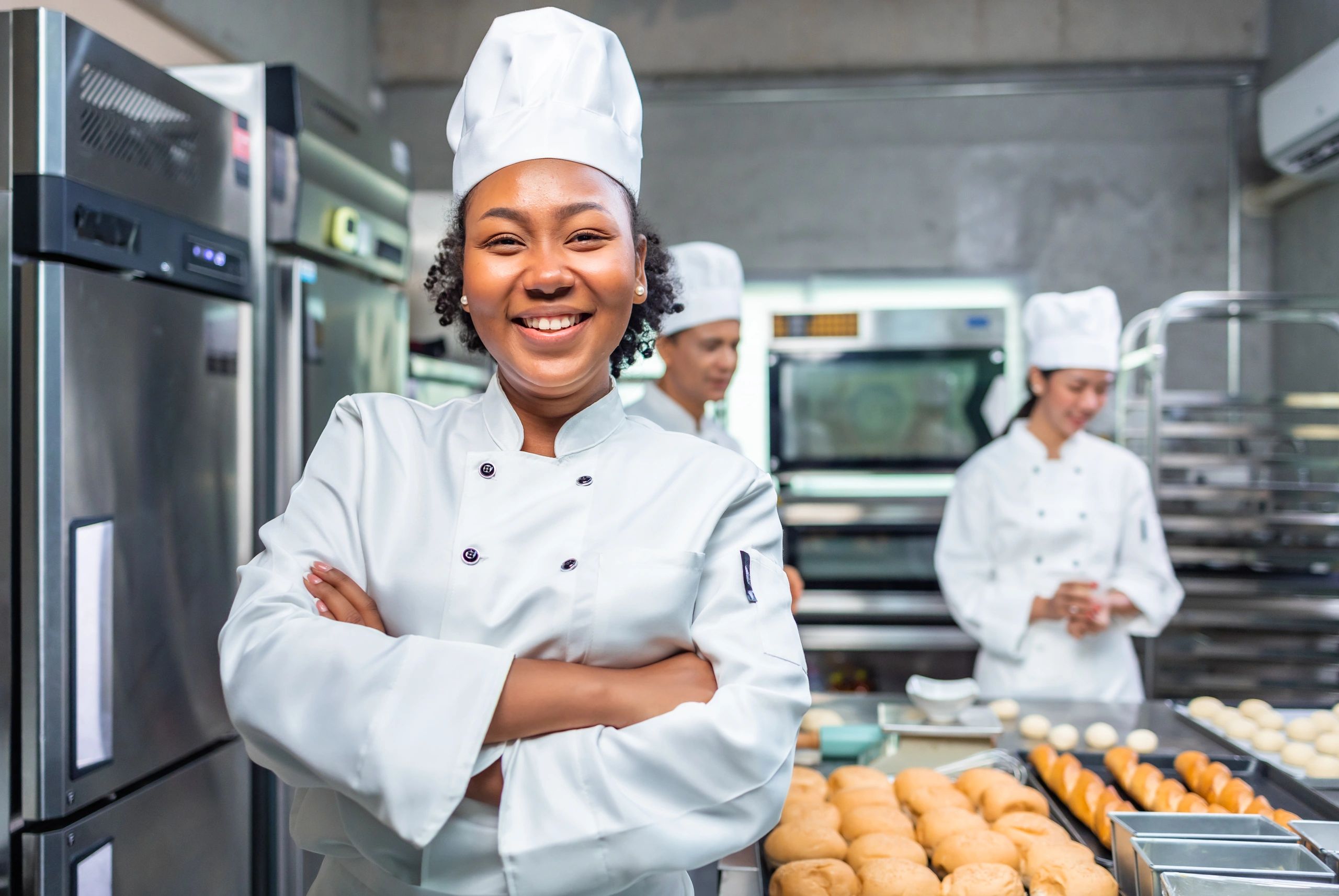 Smiling chef in a busy commercial kitchen with baked goods.