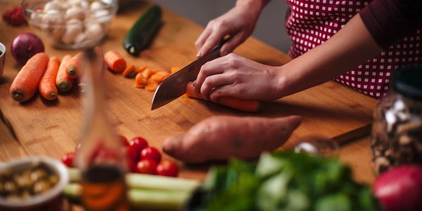 Person chopping carrots on a wooden cutting board surrounded by fresh vegetables.