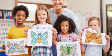 Children proudly show colorful butterfly drawings in classroom with smiling teacher.