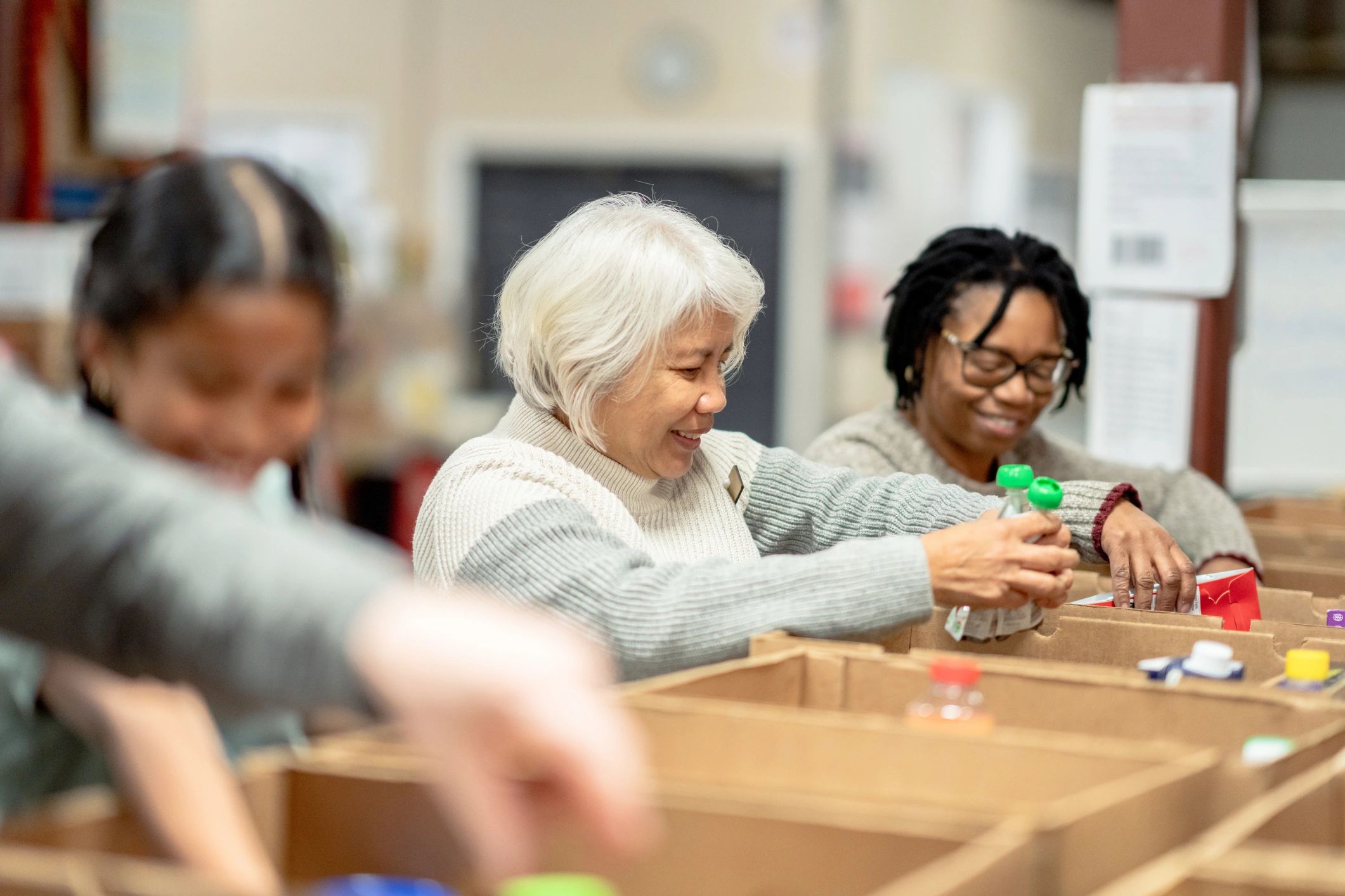 Three people packing items into boxes with smiles.