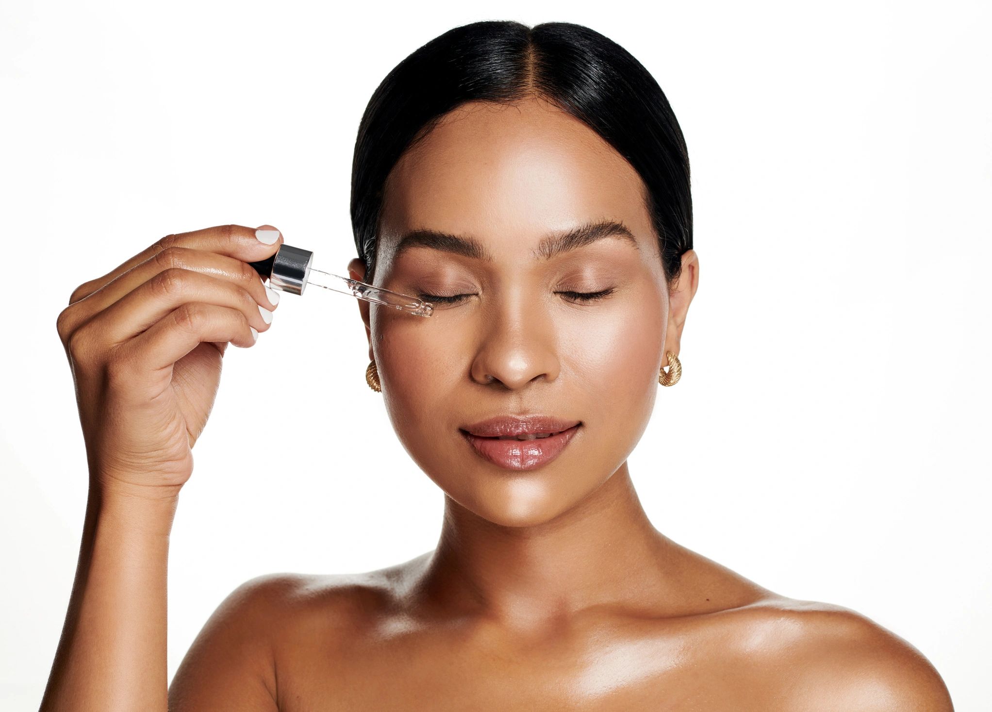 Woman applying essential oil to her face with a soft smile.