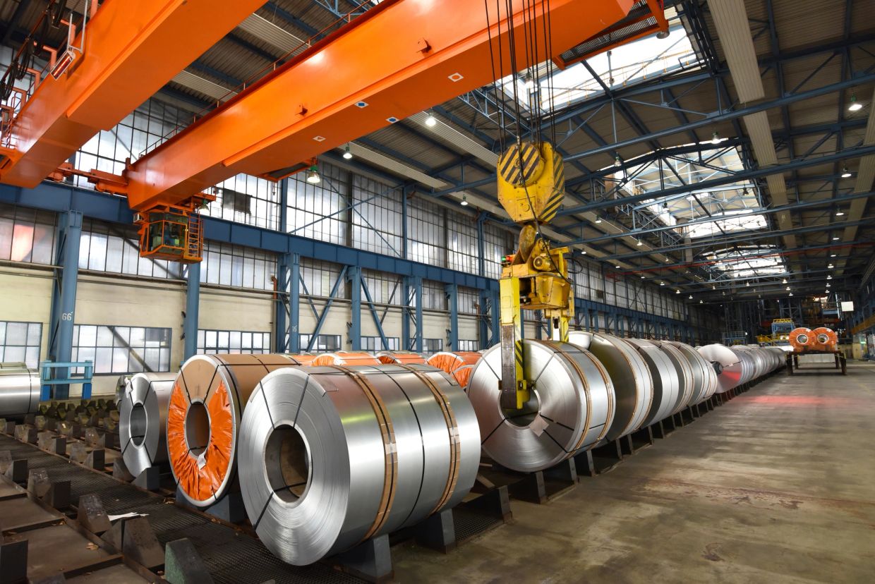Large steel coils stored in a spacious industrial warehouse with an overhead crane.